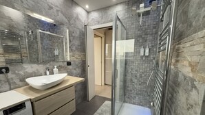 Une salle de bain moderne avec un grand miroir, un lavabo blanc, une douche en verre et un lave-linge encastré.