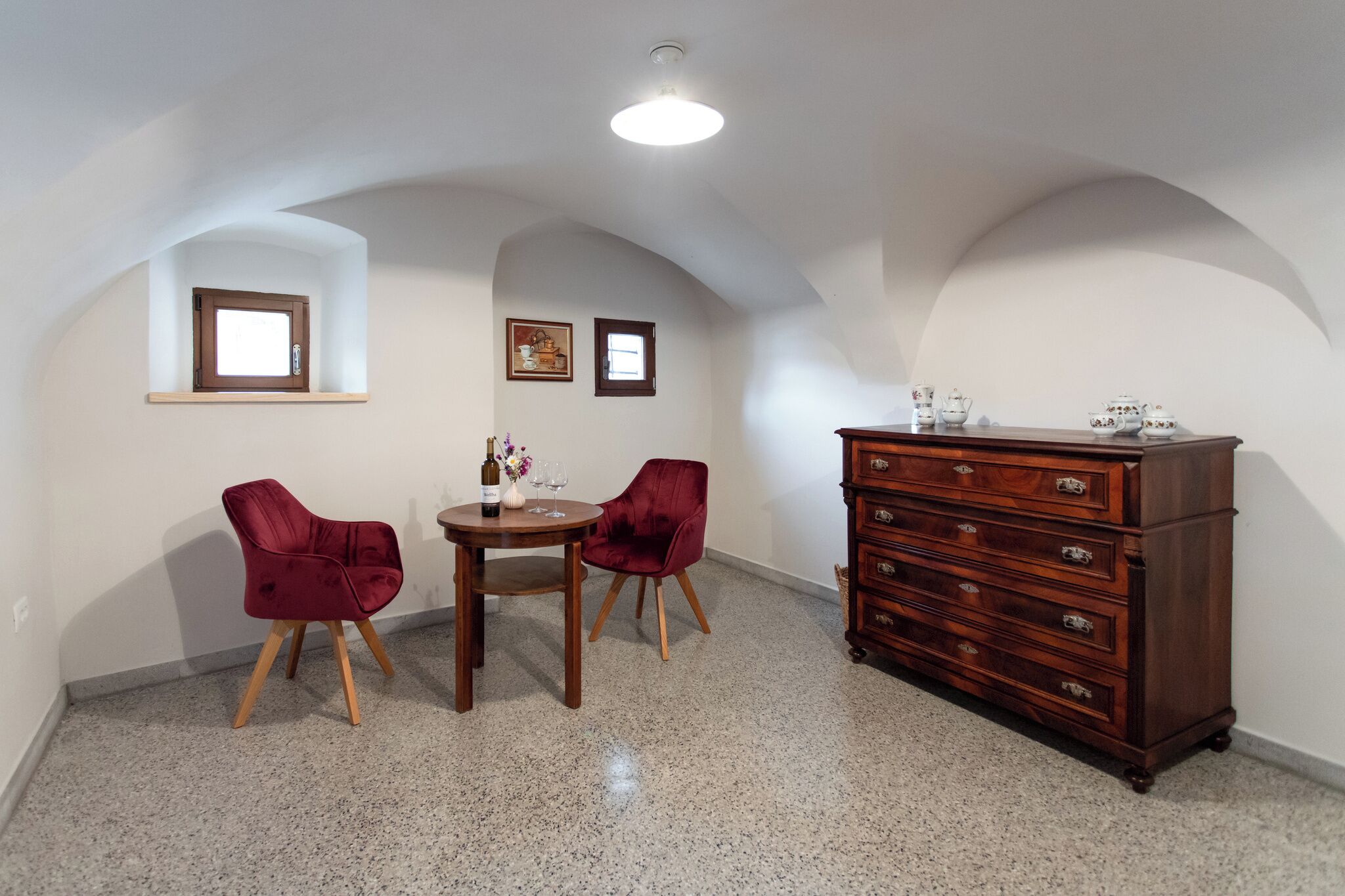 A room with a dining table, two chairs, a dresser, and a small window.
