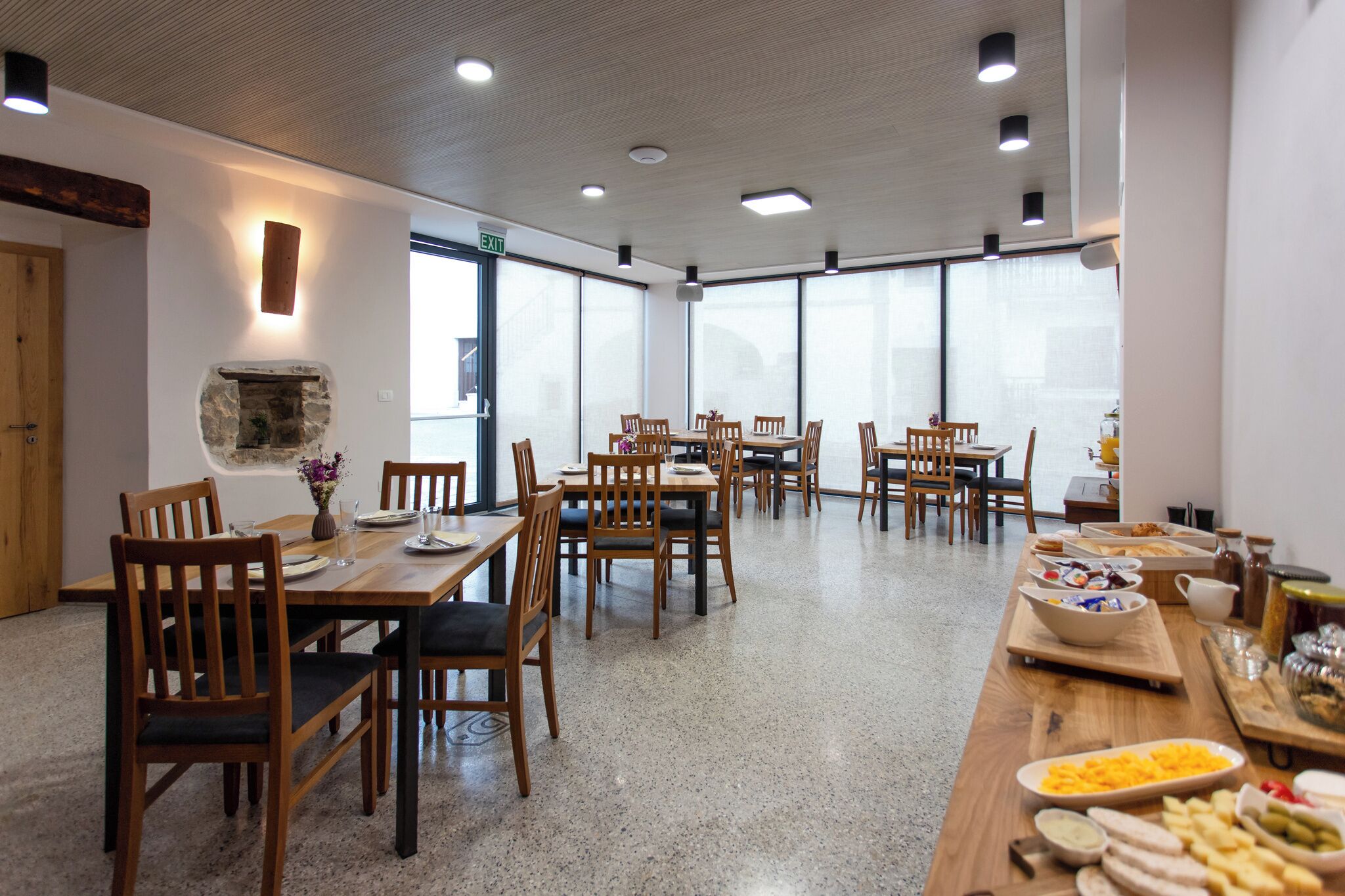 A spacious dining area with multiple wooden tables and chairs, a stone fireplace, and large windows allowing natural light.