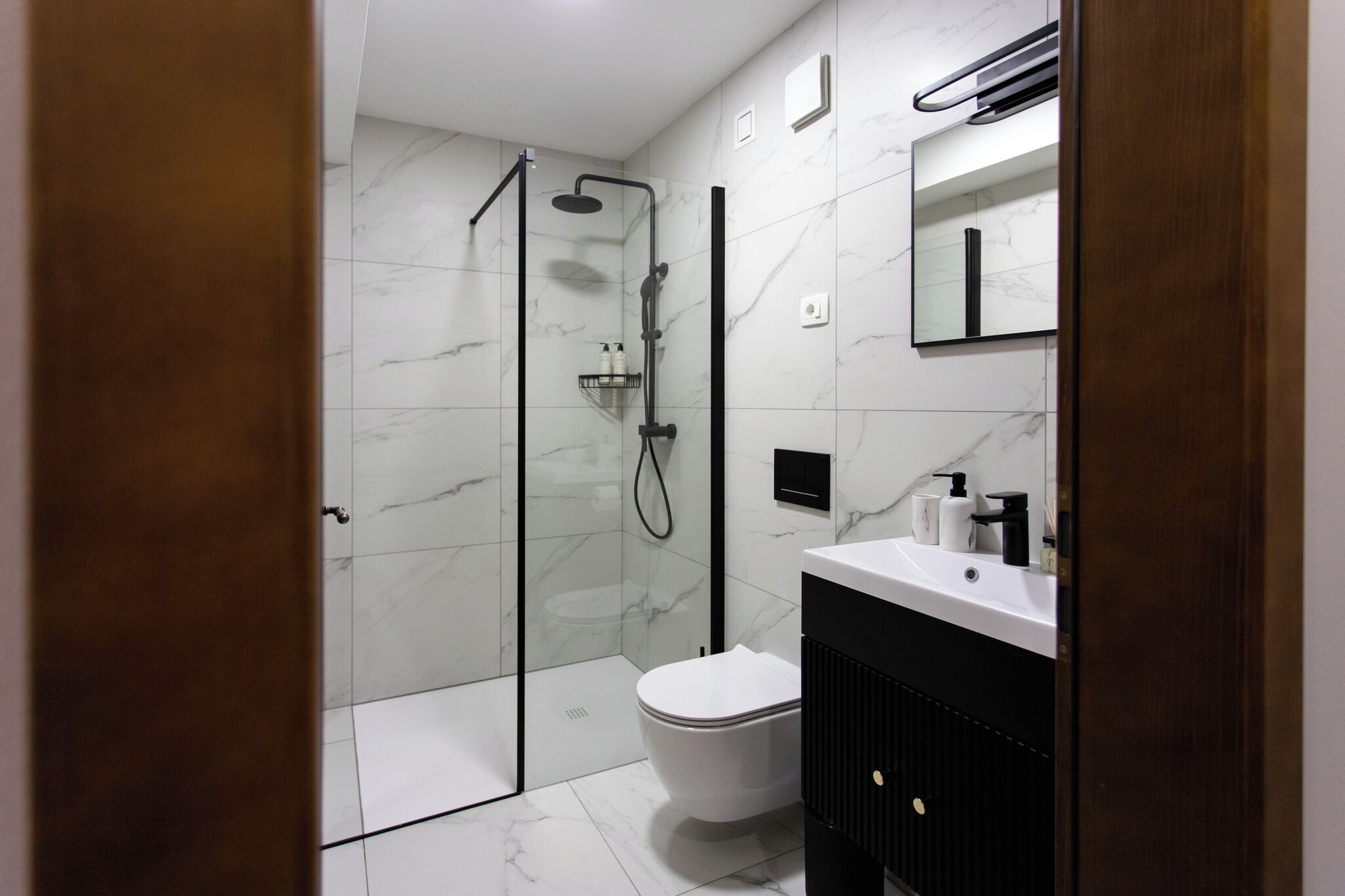 Une salle de bain moderne avec une douche à parois de verre, des toilettes blanches et un meuble-lavabo noir avec un miroir.