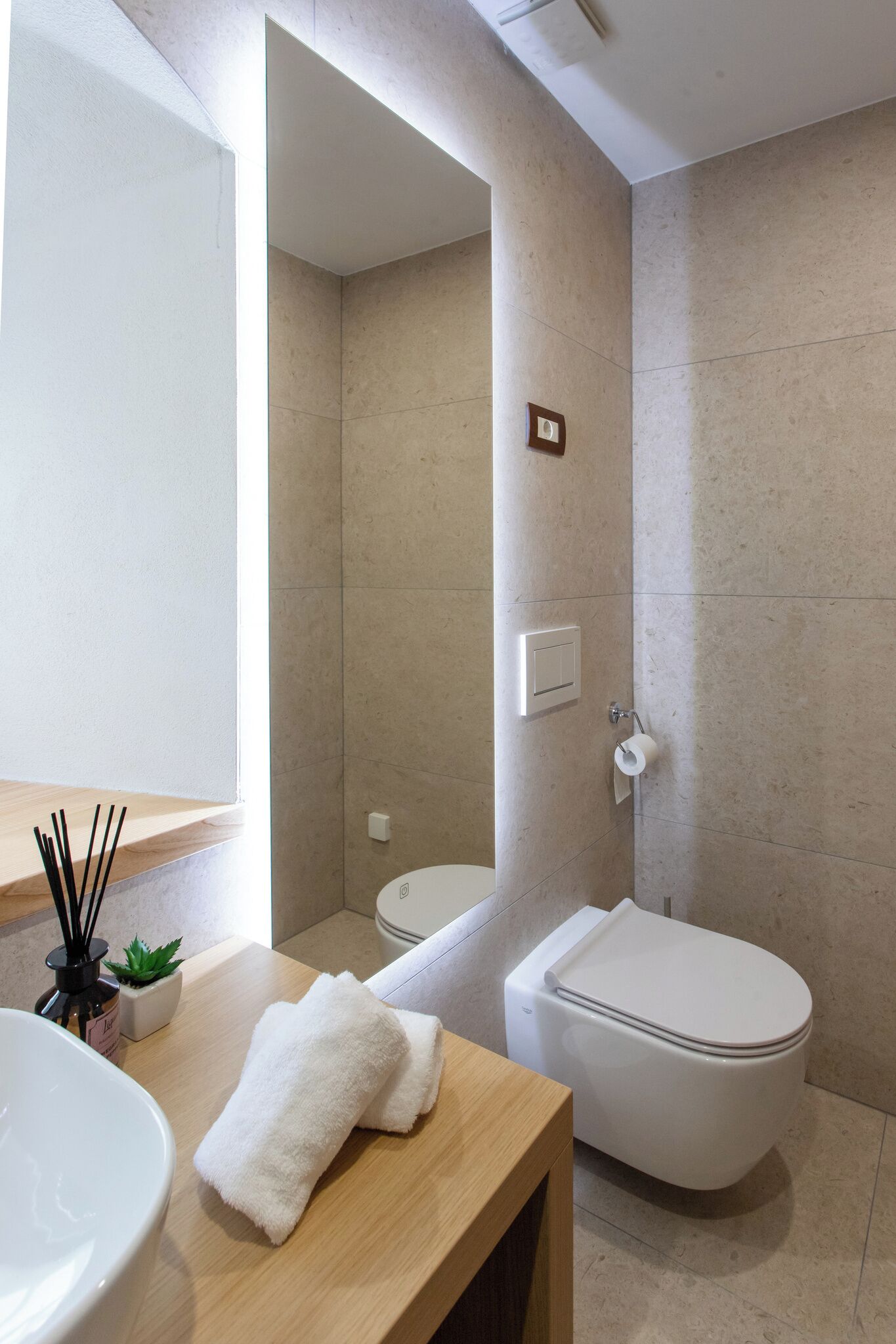 Un baño moderno con un espejo grande, un lavamanos blanco, un inodoro y un mueble de tocador de madera.
