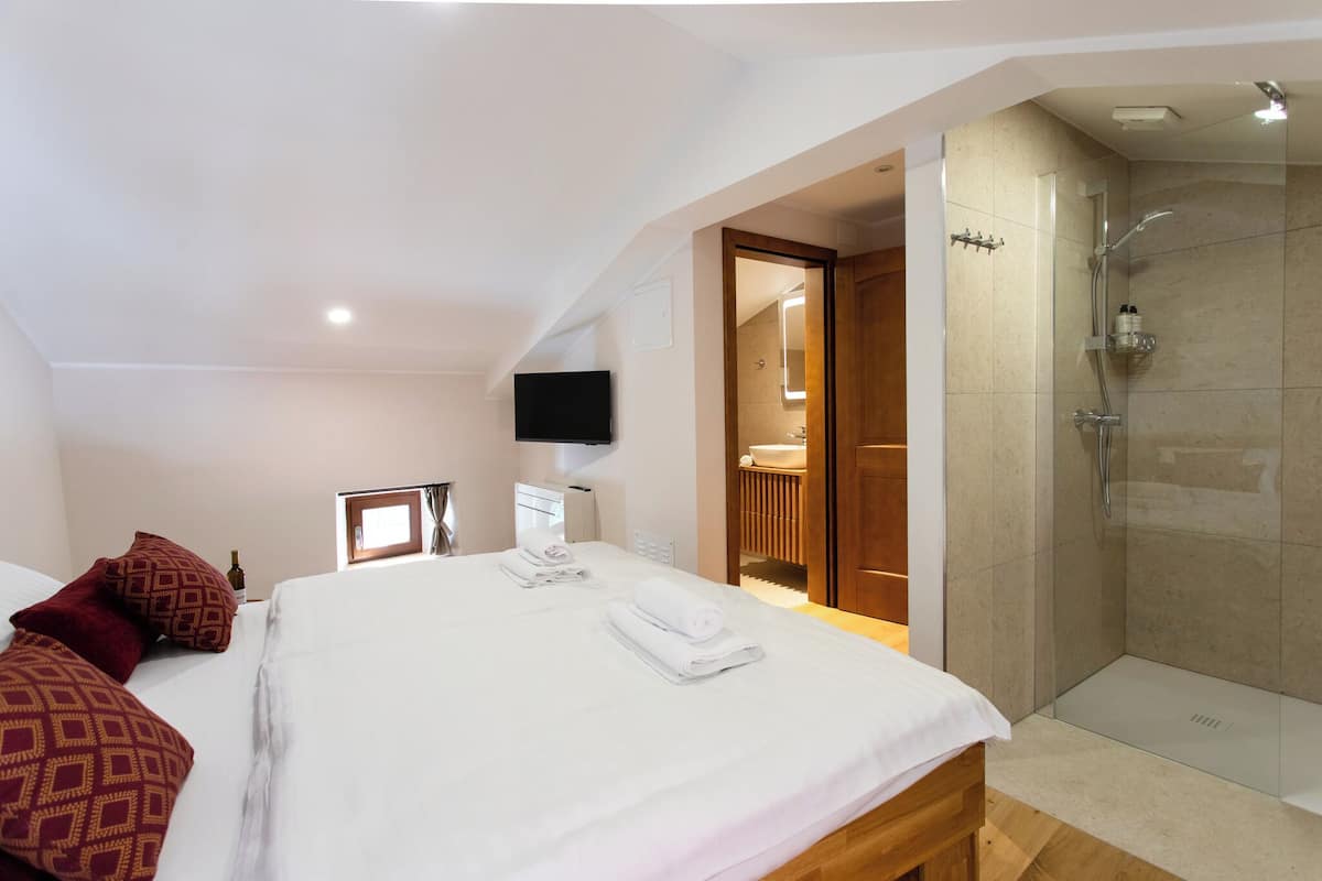 Quarto de hotel com uma cama, televisão, chuveiro e banheiro visíveis por uma porta aberta.