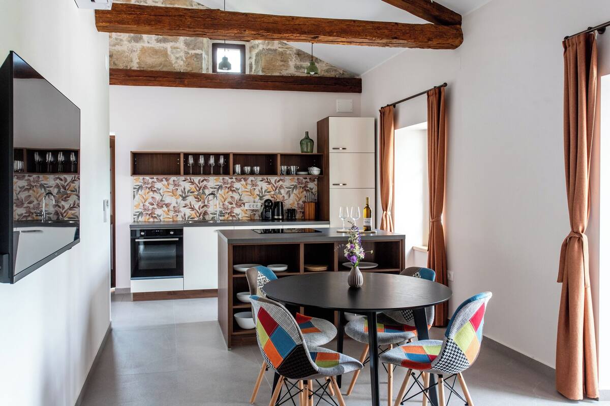 Uma cozinha moderna com ilha central, vigas de madeira e painel de azulejos.