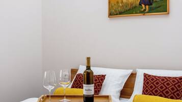 A hotel room with a bed, a painting of a woman in a field, a tray with a bottle of wine, glasses, and towels.