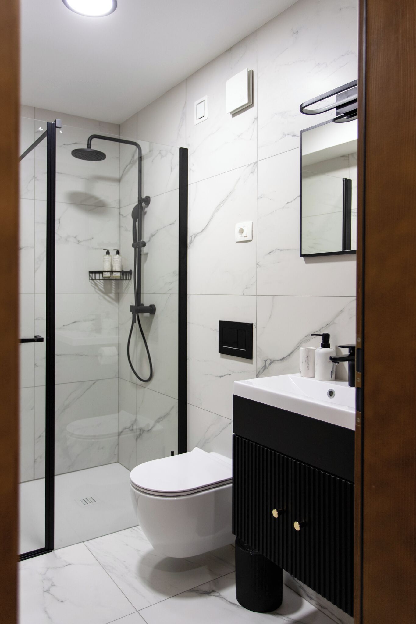 Un baño moderno con ducha envuelta en vidrio, inodoro blanco y tocador negro con espejo.