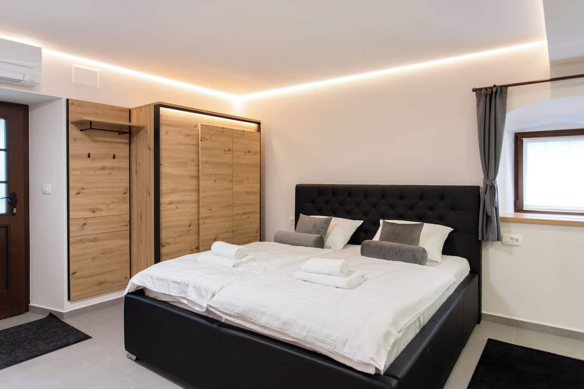 Quarto moderno com cama grande, guarda-roupa de madeira e janela com cortinas.