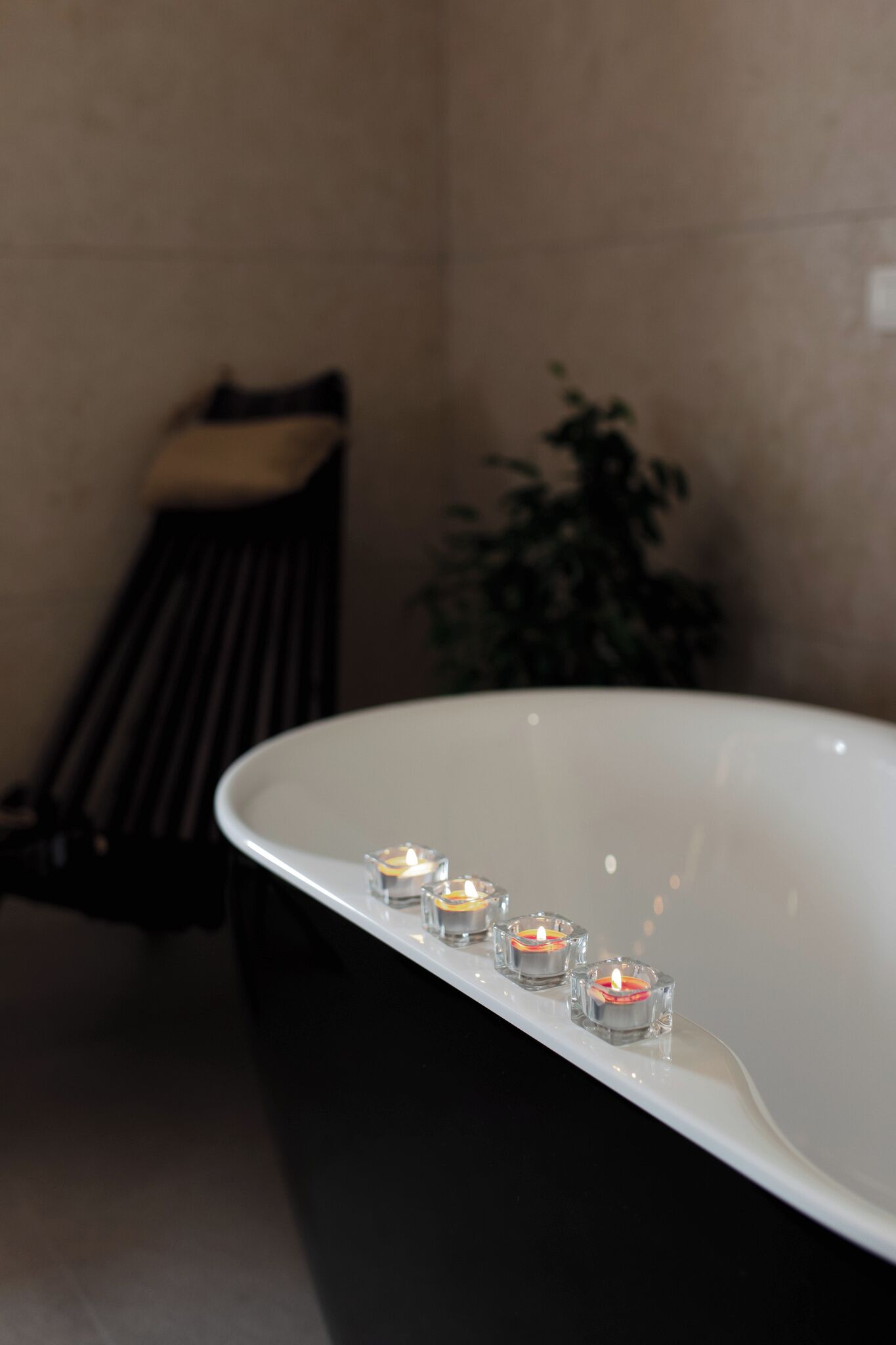 A bathtub with three lit candles, a bench, and a potted plant in a bathroom.