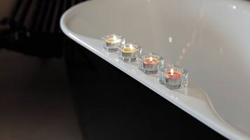 A bathtub with three lit candles, a bench, and a potted plant in a bathroom.