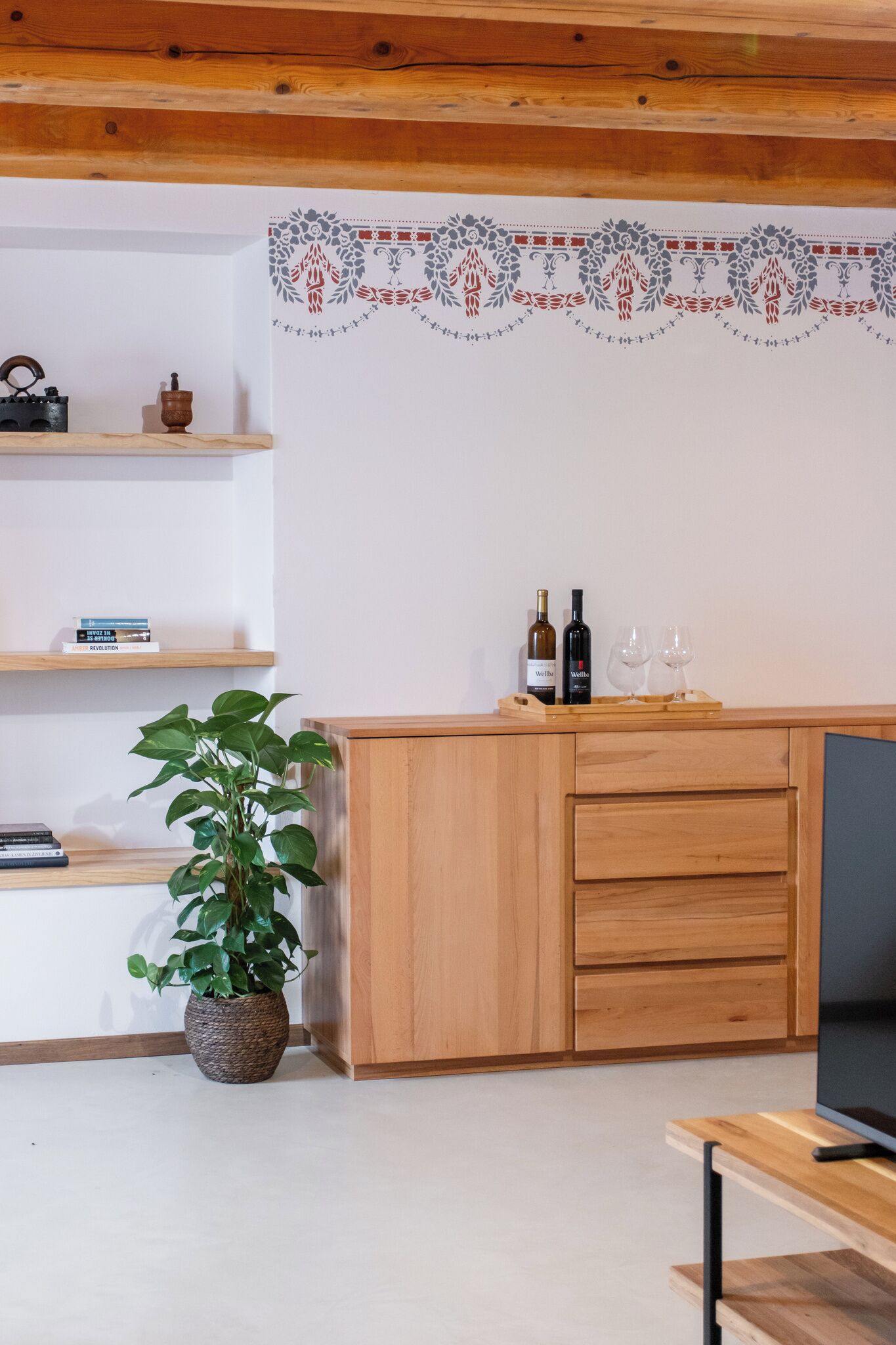 Ein modernes Wohnzimmer mit Holzmöbeln, einer Topfpflanze, einem Fernseher und einer Wandverzierungen.