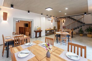 A spacious dining area with wooden tables and chairs, a staircase, and potted plants. - Wellba Boutique Hotel (Ajdovšcina)