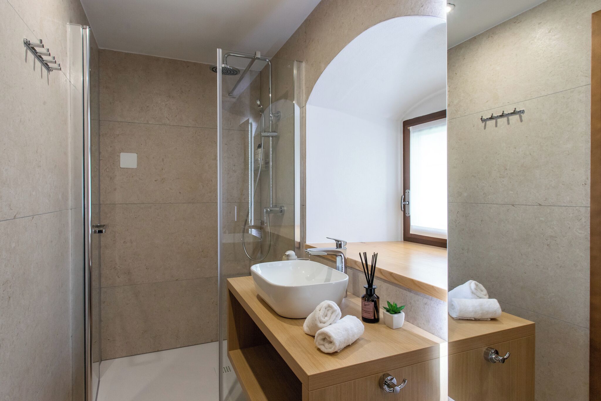 Un baño moderno con ducha de vidrio, un lavamanos grande y un mueble de tocador de madera.