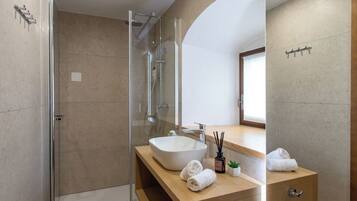 Un baño moderno con ducha de vidrio, un lavamanos grande y un mueble de tocador de madera.