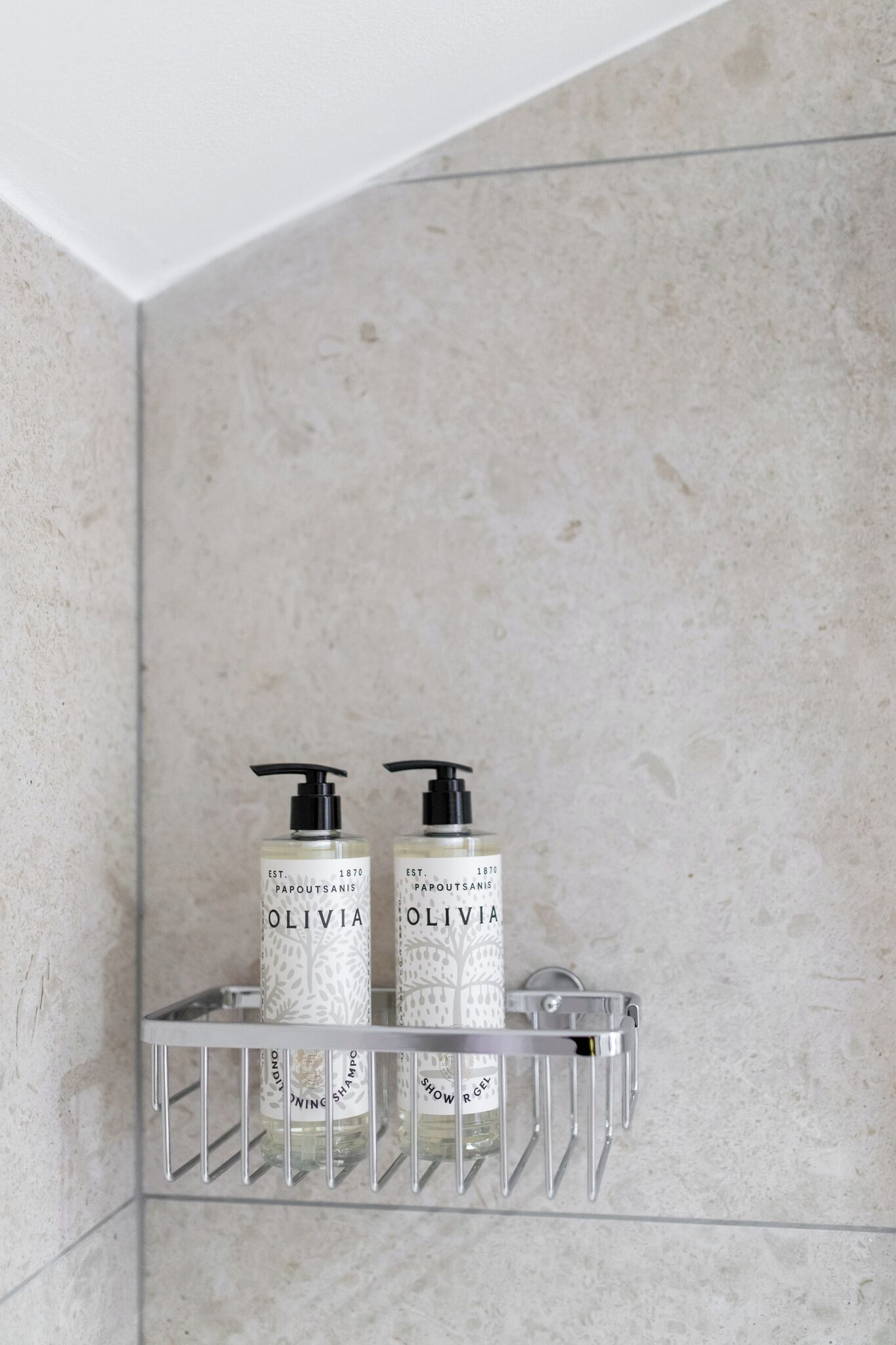 Une salle de bain avec un porte-savon pour la douche contenant deux bouteilles de gel douche Olivia.