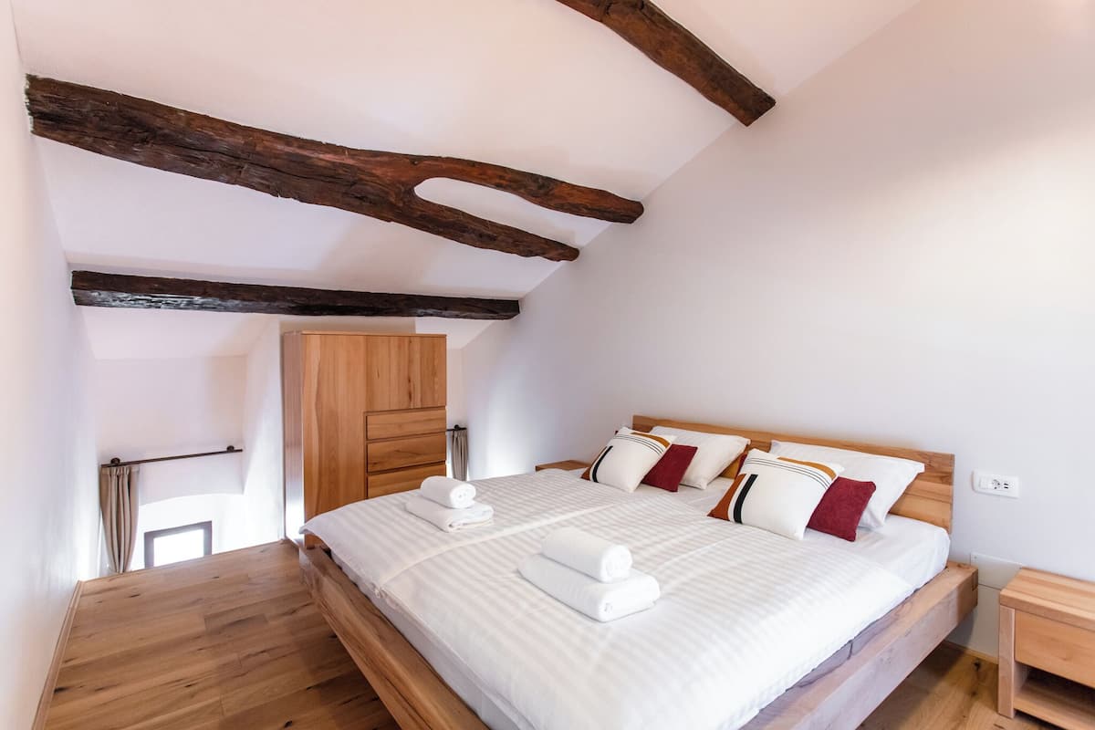 Quarto com cama de madeira, roupa de cama branca e guarda-roupa de madeira.