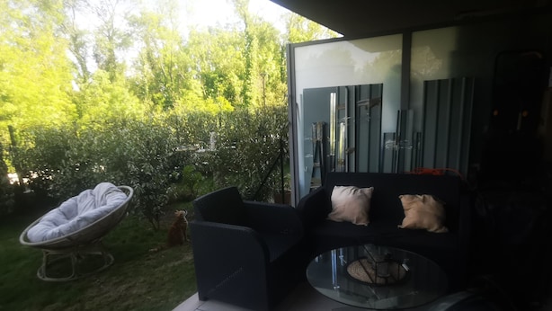 Une terrasse avec un canapé noir, une table ronde en verre et un chat.