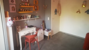 Une chambre d’enfant avec un bureau, une chaise, des étagères remplies de jouets et des décorations murales.