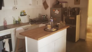 Une cuisine compacte avec des meubles blancs, un plan de travail en bois et une cuisinière intégrée. On y trouve un réfrigérateur décoré d  ’aimants et une machine à café.