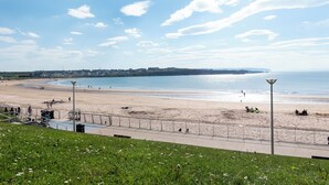A coastal beach scene with a paved walkway, a lamp post, and a distant view of the sea. - VISIT THE LOOKOUT AND EXPERIENCE THE ATLANTIC OCEAN AT ITS BEST. (Portrush)