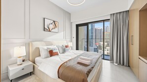 Une chambre d’hôtel moderne avec un grand lit, une table de chevet, une lampe de chevet, une œuvre d’art encadrée et une vue sur la ville par une grande fenêtre.