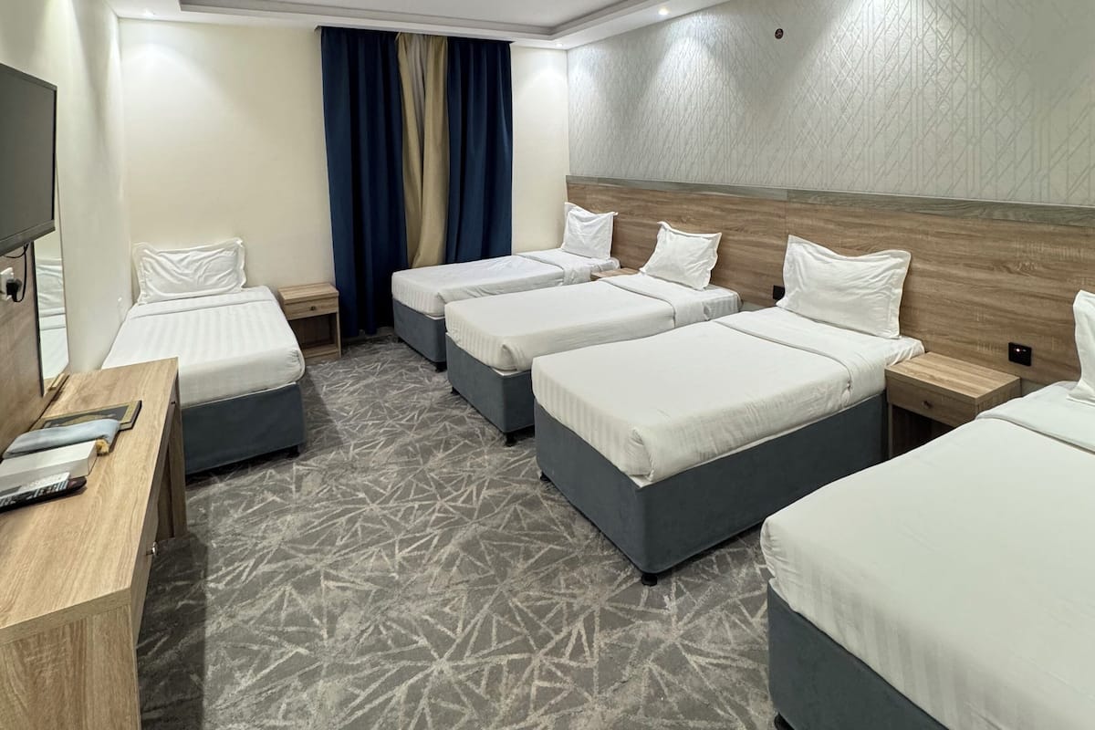 A hotel room with four single beds, a wooden desk, a flat-screen TV, and a patterned carpet.