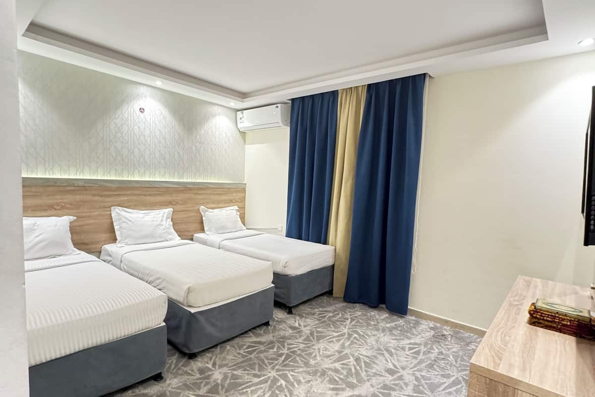 A hotel room with three beds, an air conditioning unit, a patterned carpet, and a wooden side table.
