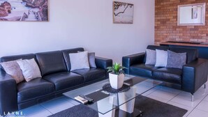 Una sala de estar moderna con dos sofás de cuero negro, una mesa de centro de vidrio y una pared decorativa de ladrillo.