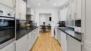Una cocina moderna con armarios blancos, suelo de madera y una isla central con asientos.