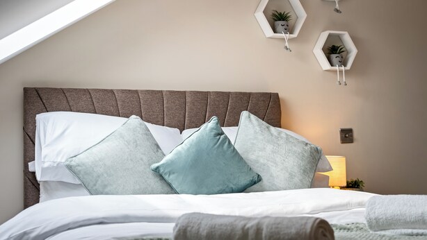 Un dormitorio con techo inclinado, una cama con ropa de cama blanca y turquesa, y tres repisas hexagonales con plantas en macetas.