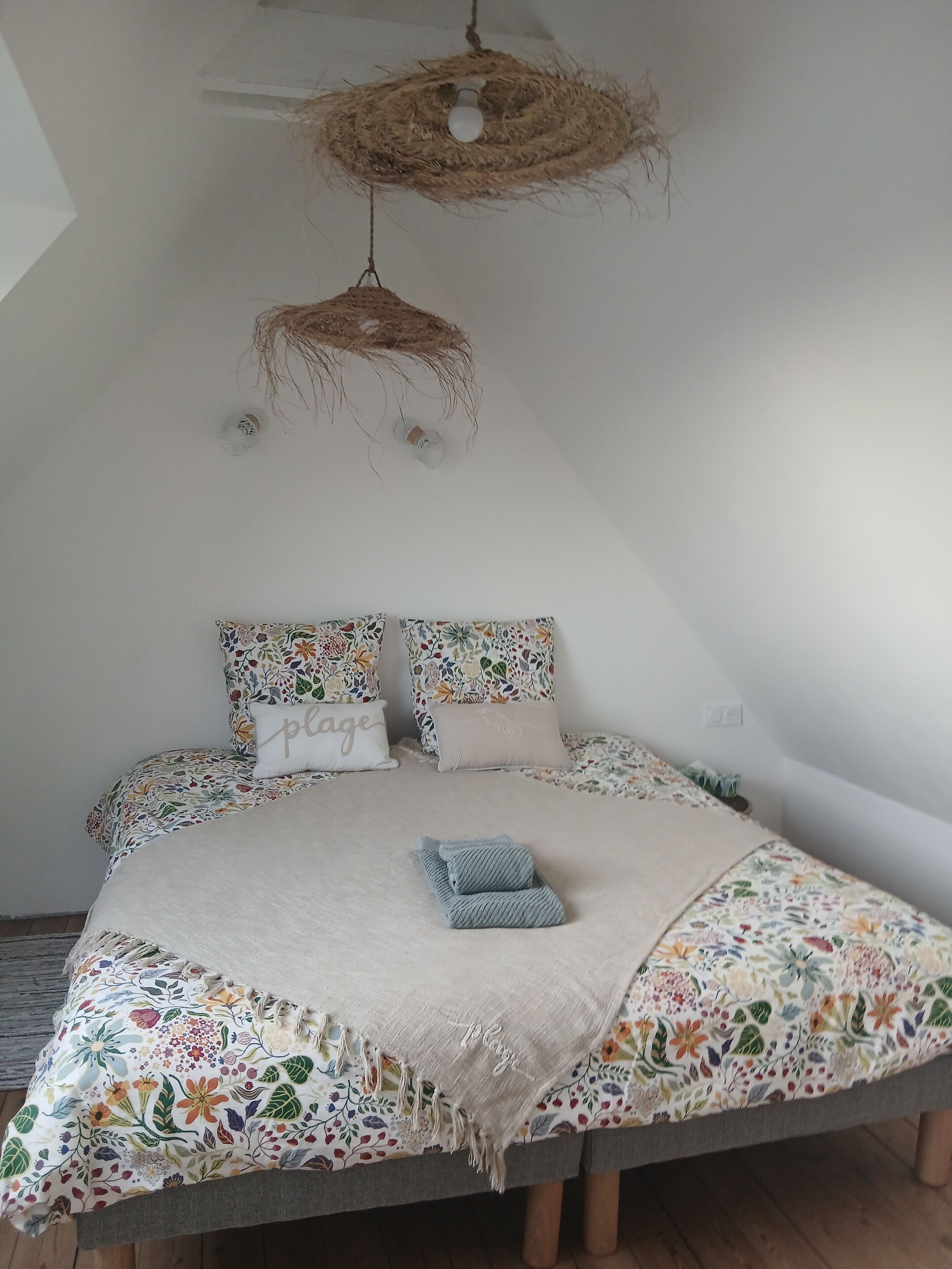 Une chambre à coucher avec un lit, une literie à motifs floraux, un luminaire suspendu en rotin et un éclairage fixé au plafond.