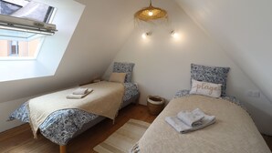 Une chambre avec deux lits, une lucarne, un luminaire en fibres tressées et une petite fenêtre.
