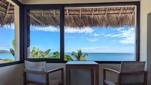 A room with a large window overlooking a beach, two wooden chairs, and a small table. - Oceanfront Luxury Villa with Infinity Pool and Private Beach (Nosy Be)