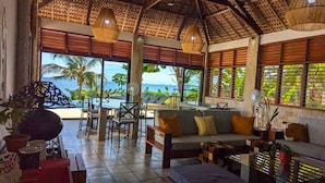 A spacious living area with a view of the ocean, a thatched roof, and a comfortable seating arrangement. - Oceanfront Luxury Villa with Infinity Pool and Private Beach (Nosy Be)