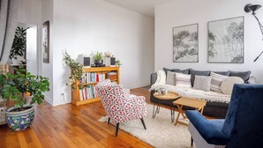A modern living room with a grey sofa, a patterned armchair, a wooden bookshelf, and a coffee table.