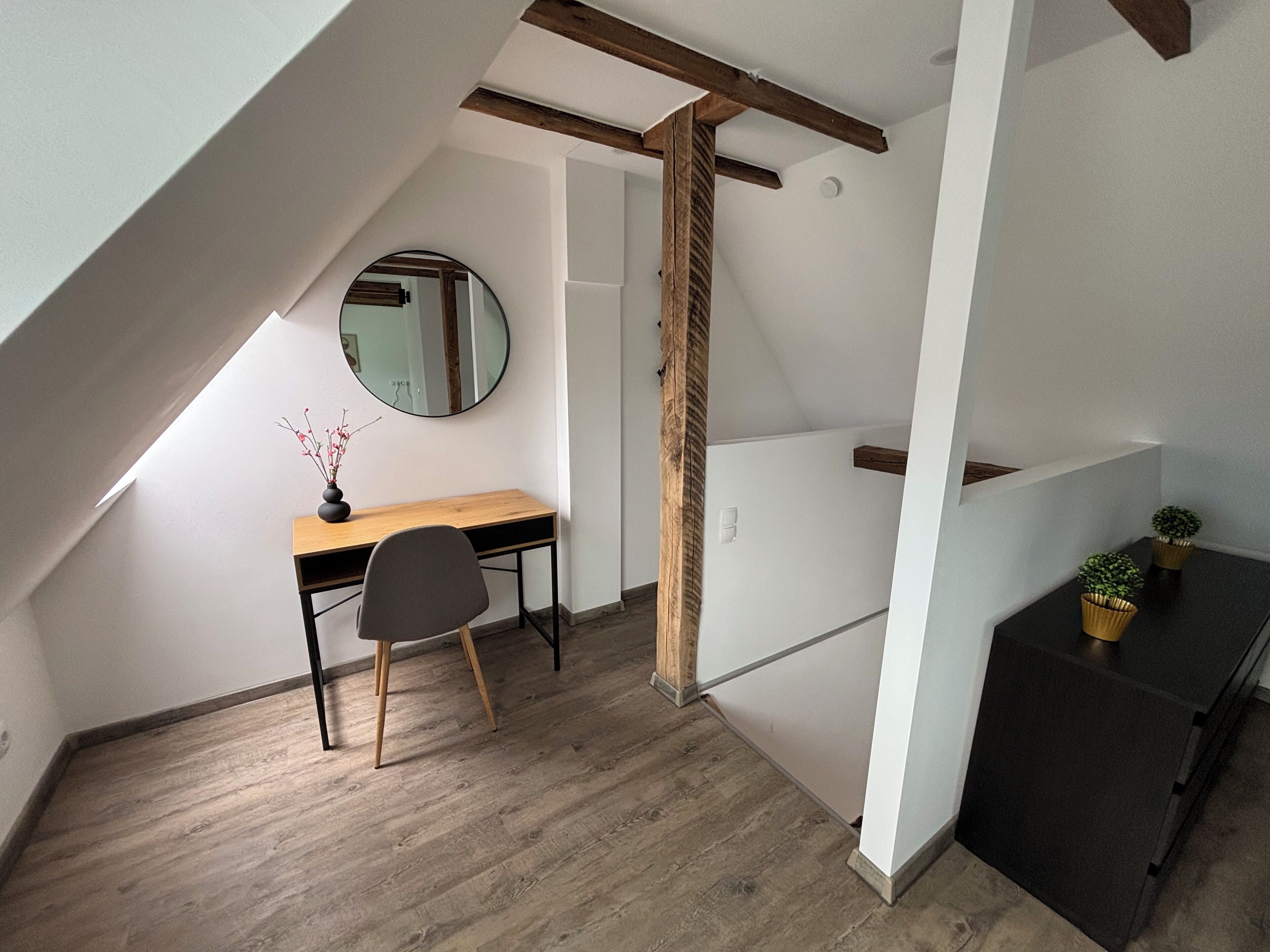 A small, sloped ceiling room with a desk, chair, and a mirror.