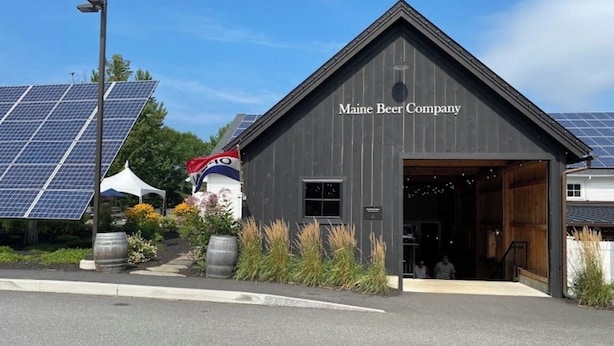 A building labeled "Maine Beer Company" with a large open garage door, solar panels, and a tent with a flag. - Quintessential Maine- 
Spacious Home, Close to Town, Vacationland all around you (Freeport)