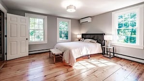 A bedroom with a bed, two windows, a bedside table, a nightstand, and a door. - Quintessential Maine- 
Spacious Home, Close to Town, Vacationland all around you (Freeport)