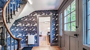 A hallway with a wooden staircase, patterned wallpaper, and a view into a room with a radiator. - Quintessential Maine- 
Spacious Home, Close to Town, Vacationland all around you (Freeport)