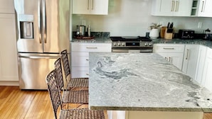 A modern kitchen with white cabinets, stainless steel appliances, and a granite island. - Quintessential Maine- 
Spacious Home, Close to Town, Vacationland all around you (Freeport)