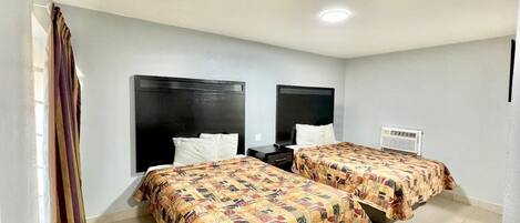 Une chambre d’hôtel avec deux lits, chacun recouvert d’une couvre-lit à motifs, une table de chevet, un téléviseur et un climatiseur fixé au mur.