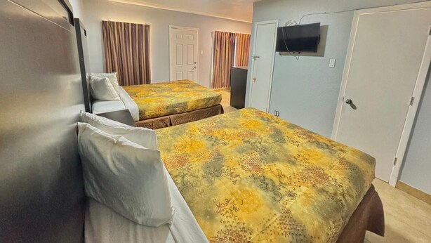 A hotel room with two beds, a TV mounted on the wall, and a door with a speaker. - Welcome Motel (Killeen)