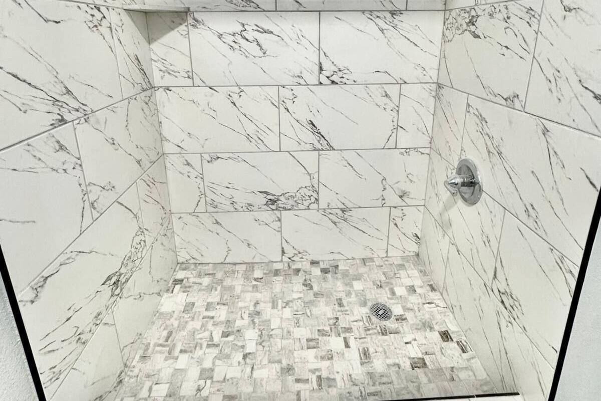 A shower with marble tiles and a mosaic floor.