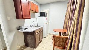 A compact kitchen with a sink, a refrigerator, and a microwave. There is a small wooden table and a chair. - Welcome Motel (Killeen)