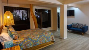 Un dormitorio con una cama, un sofá azul, un ventanal grande y un televisor montado en la pared.