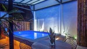 Un área de piscina con mesa y sillas de madera, rodeada de vallas de bambú y plantas.
