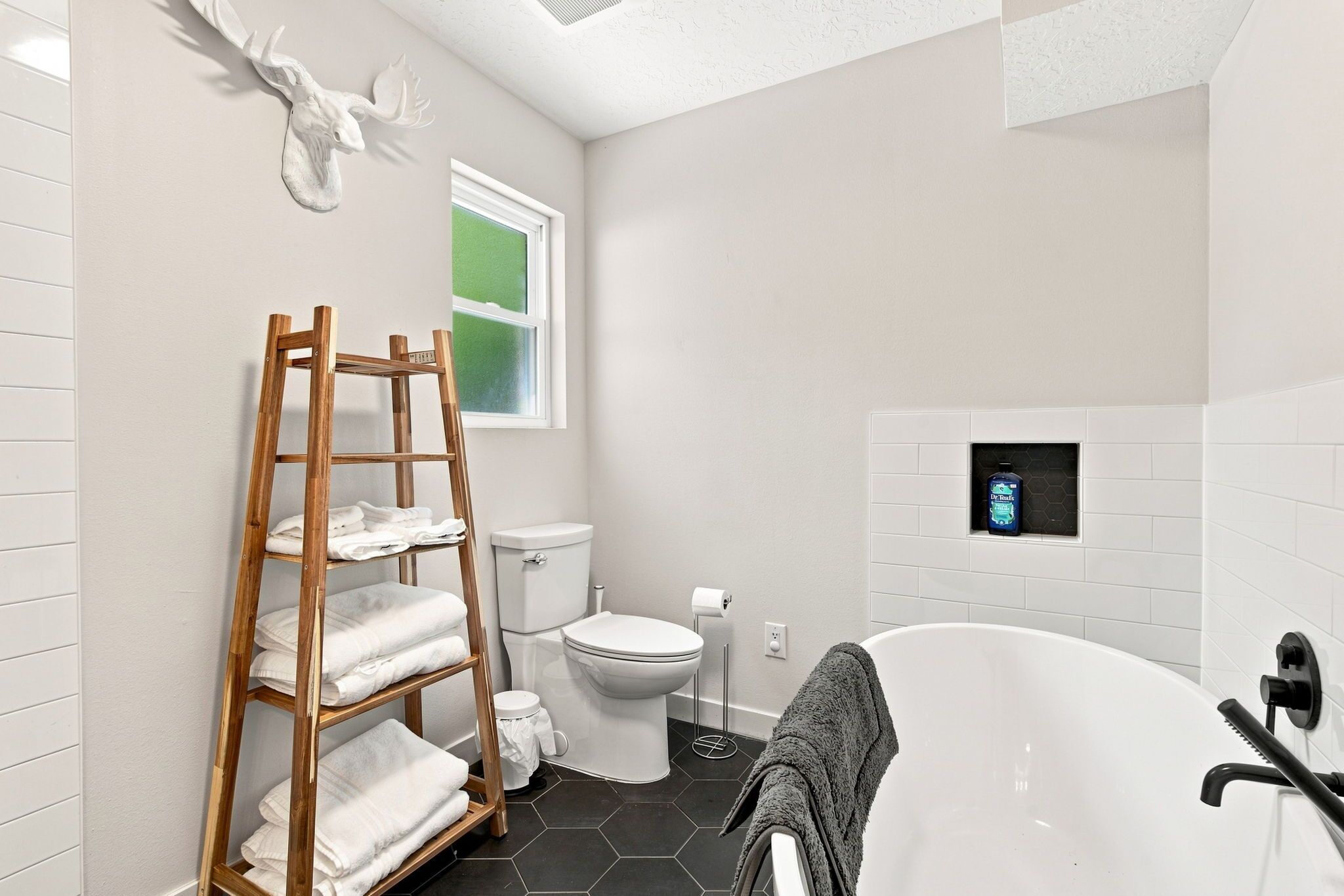 A modern bathroom with a wooden towel rack, toilet, and a bathtub.