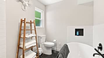A modern bathroom with a wooden towel rack, toilet, and a bathtub.