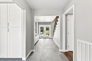 A hallway with white walls, grey tiled flooring, and a staircase with black railings.