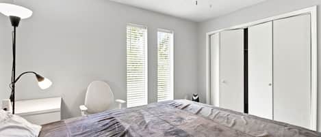 A bedroom with a bed, a desk, a chair, a wardrobe, and a ceiling fan.