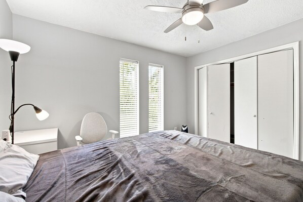A bedroom with a bed, a desk, a chair, a wardrobe, and a ceiling fan.