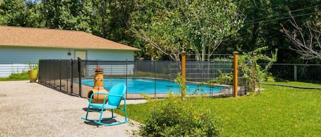 Un patio trasero con piscina, un área de patio techado y un jardín cercado.